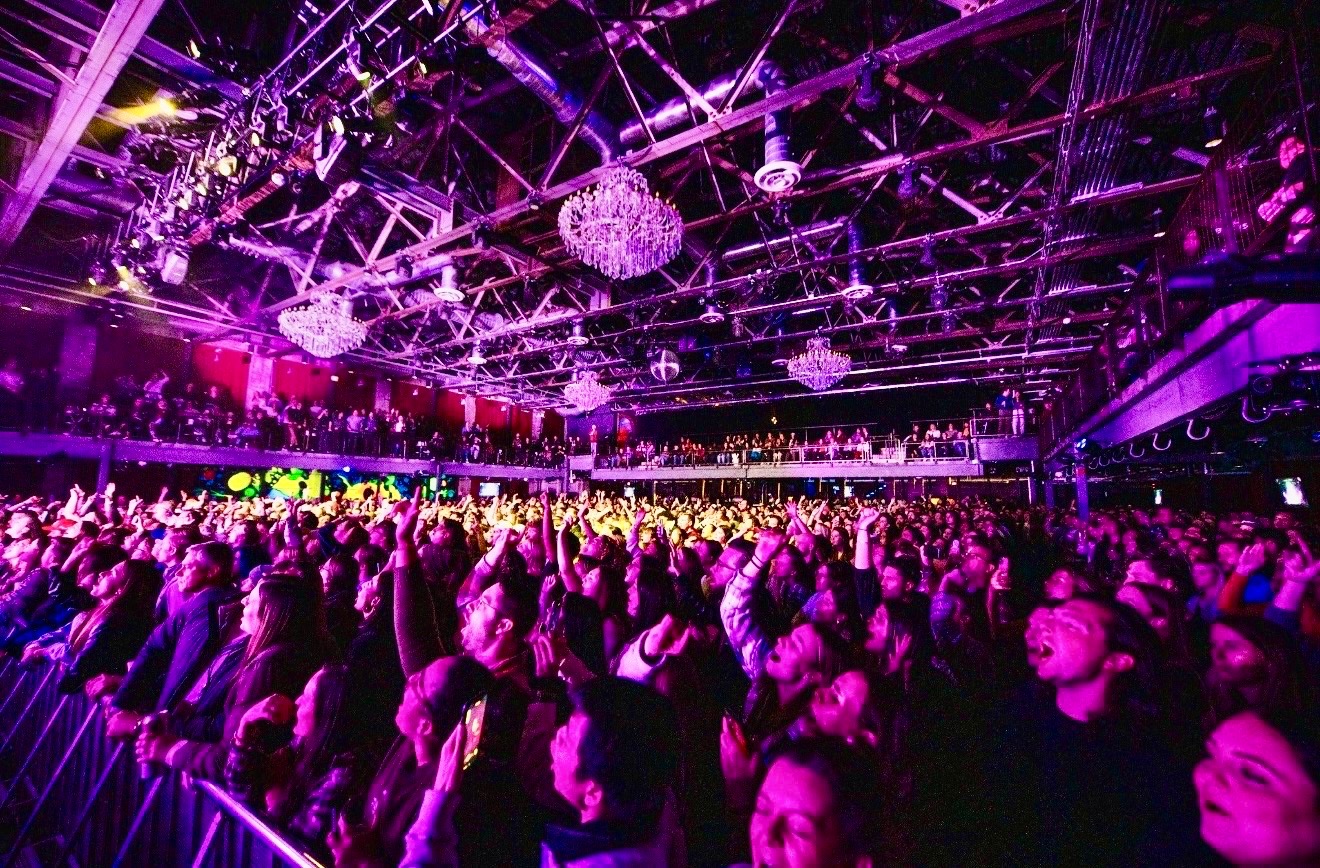 A packed live concert crowd beneath colorful stage lights in Philadelphia